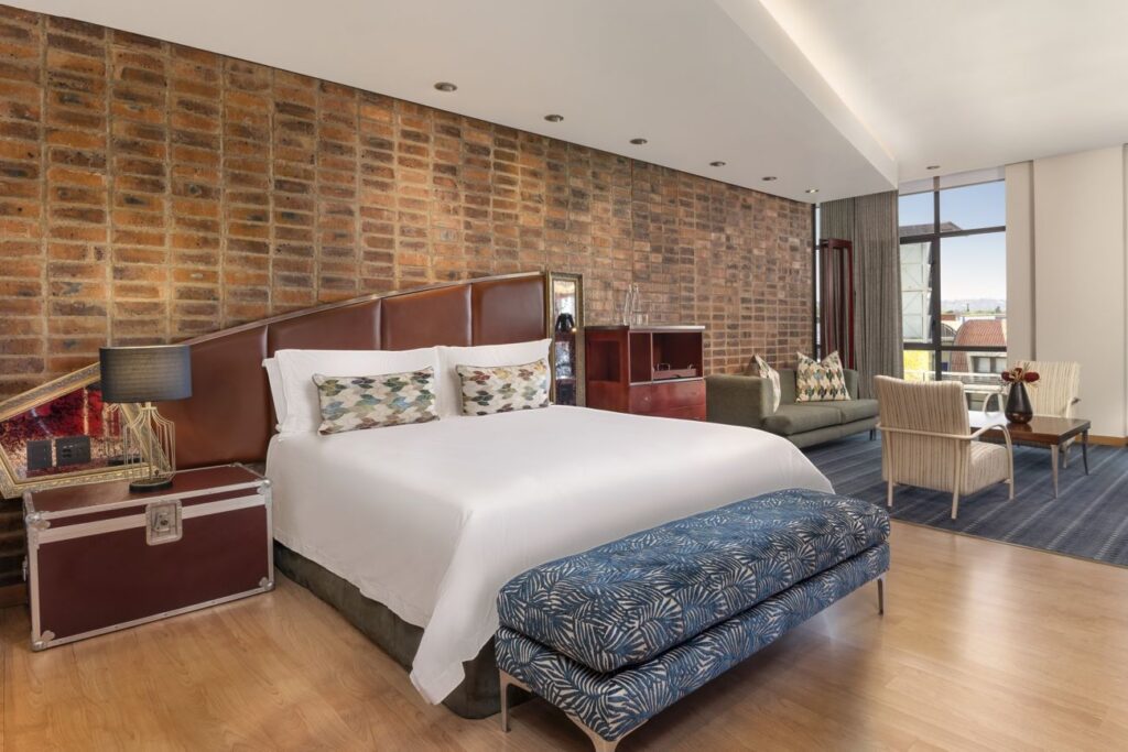 African Pride Melrose Arch, Autograph Collection – King bed, bench, and lounge area