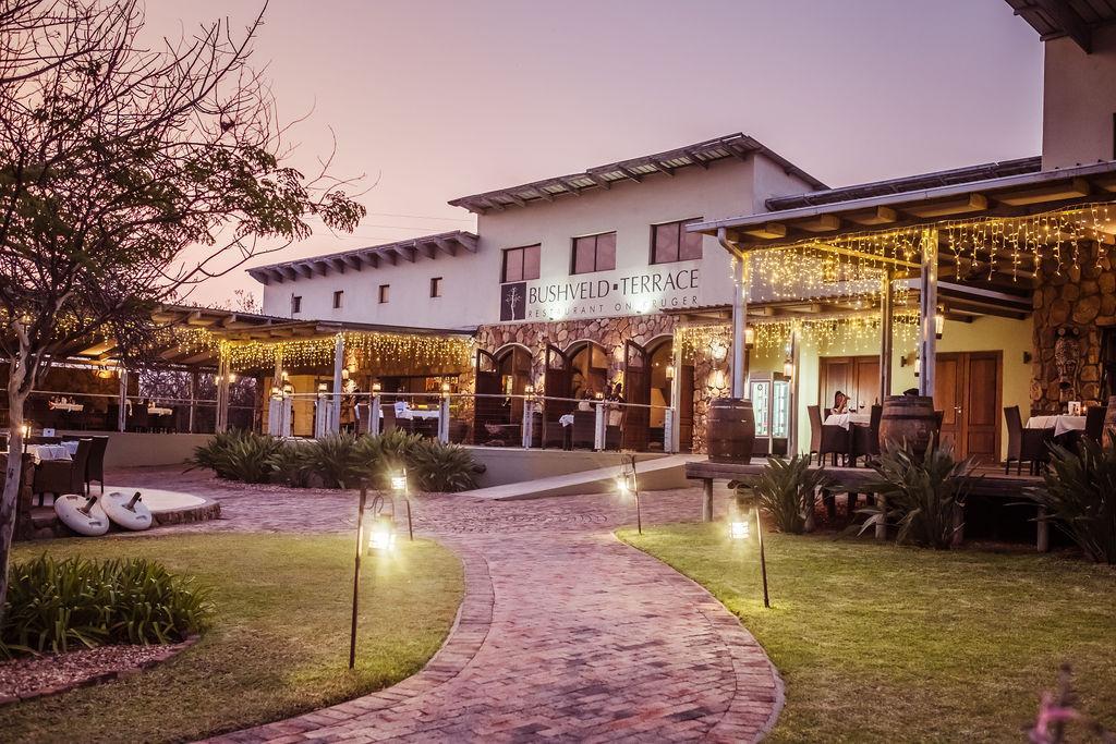 Bushveld Terrace Hotel at dusk, with its lit terrace restaurant and a lantern-lined garden path