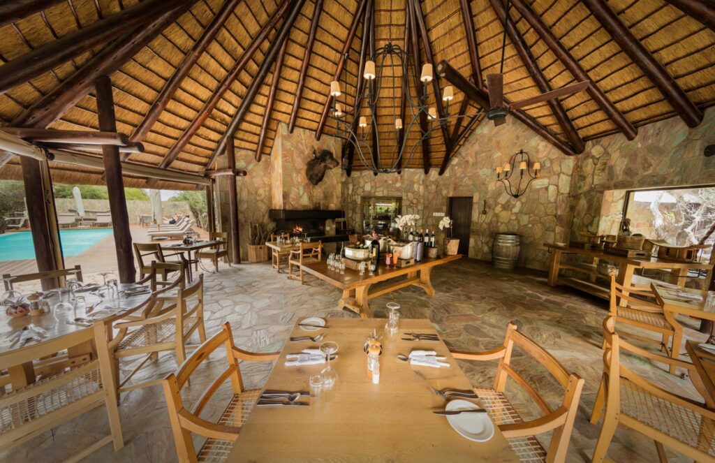 Kapama Buffalo Camp dining area under thatch, with stone walls and a view of the pool
