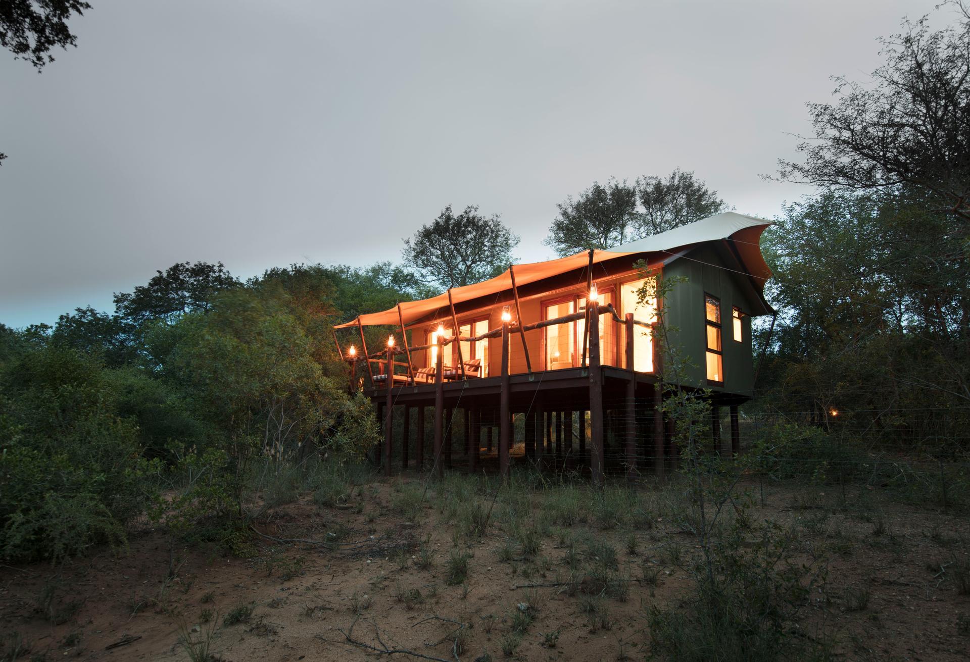 Raised luxury tent at Kapama Buffalo Camp, lit at dusk among the trees