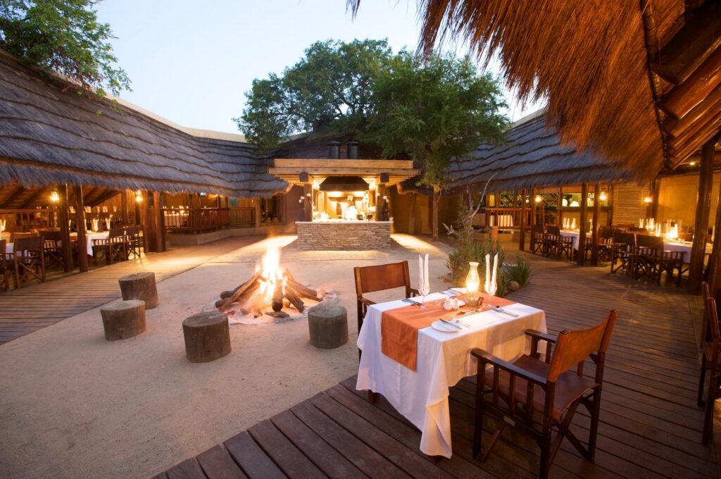 Kapama River Lodge boma with a fire and tables set for dinner at dusk