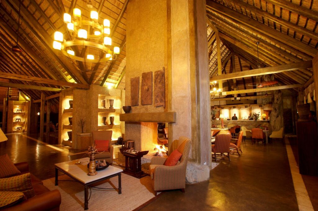 Kapama River Lodge lounge under a thatched roof, with a fireplace and chandelier