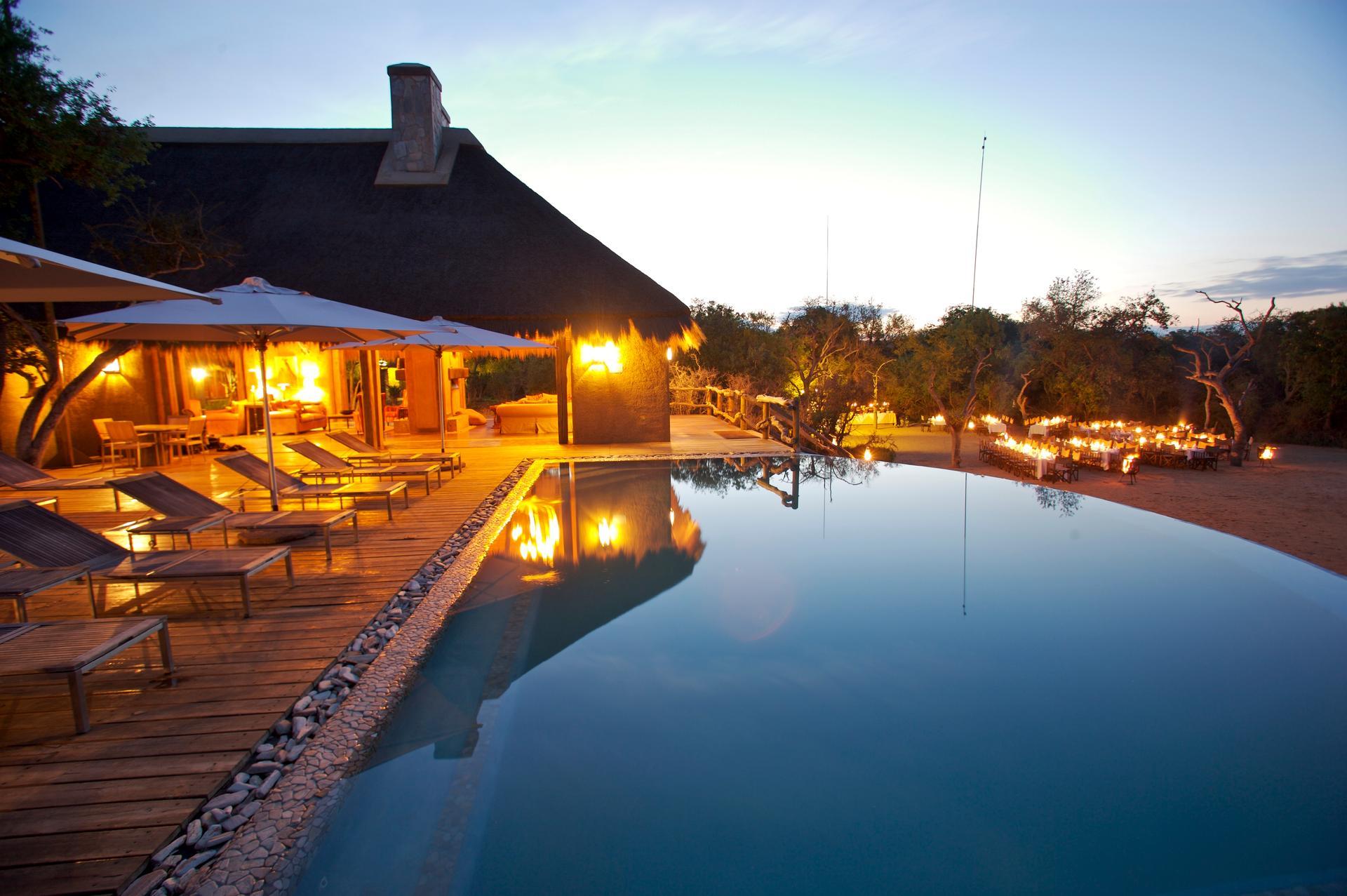 Kapama River Lodge swimming pool and thatched main building at dusk
